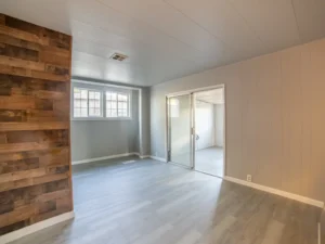 An empty room in a home with light grey walls, light wood flooring, and a rustic wooden accent wall, showcasing real estate photo editing.